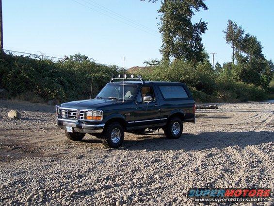 1995 Ford Bronco parked on a gravelly surface with trees and a fence in the background