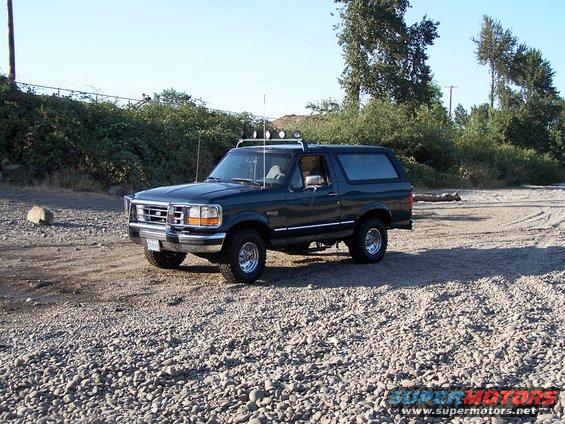 Dark green Ford Bronco parked on a gravel lot with trees and a fence in the background