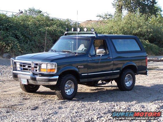 Dark green 1992 Ford Bronco SUV with roof rack and spotlights, parked on gravel