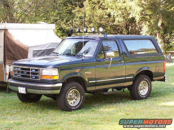 Dark green Ford Bronco parked on grass with a pop-up camper behind it