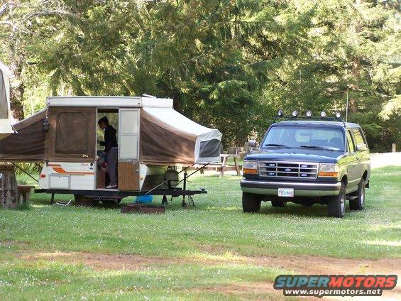 Dark blue Ford Bronco parked on grass next to a pop-up camper