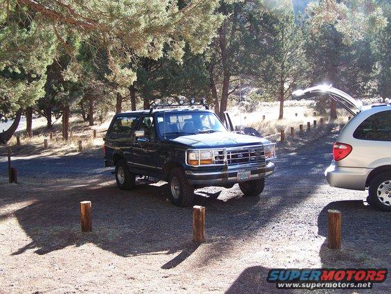 1995 Ford Bronco parked in a wooded area with a silver minivan nearby