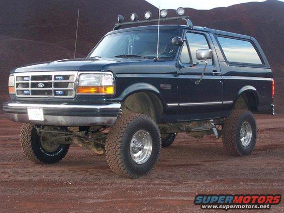 Dark blue Ford Bronco with off-road tires and roof lights parked on dirt
