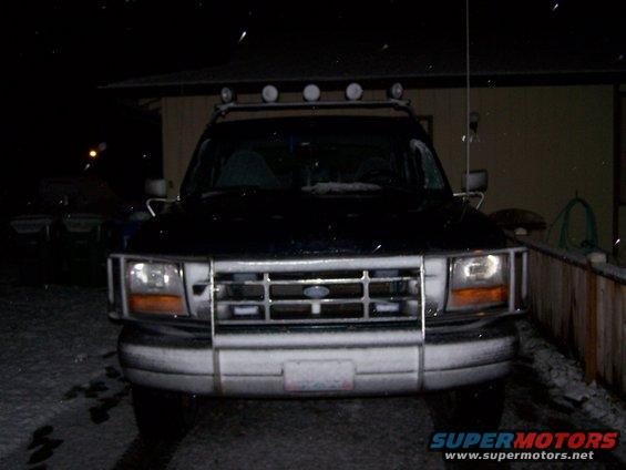 Black Ford Bronco with a chrome grille and light bar, covered in snow