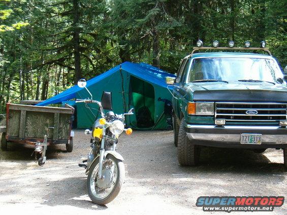 Green Ford truck parked next to a blue tent and a motorcycle. Trailer also visible