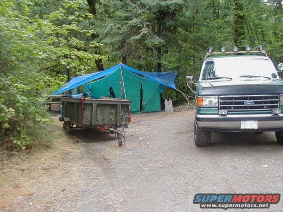 Green Ford F-Series truck with roof lights parked on a gravel road next to a tent and trailer