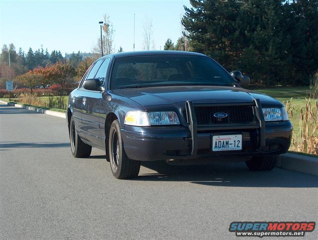 Dark blue 2001 Ford Crown Victoria police car with a push bar, parked on asphalt