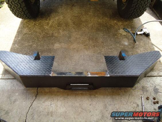 Custom steel bumper with winch mount and diamond plate accents. Tools and parts are scattered around