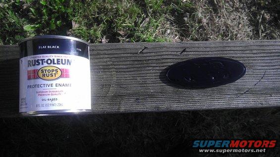 Black Ford oval emblem on weathered wood next to a can of Rust-Oleum flat black paint