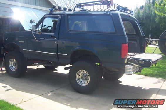 Dark green SUV with roof rack, lifted suspension, and hood open. Rear tailgate is down