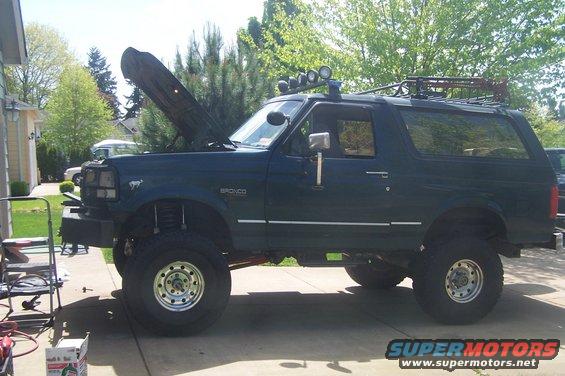 Dark green lifted Ford Bronco with roof rack and hood open, parked on driveway