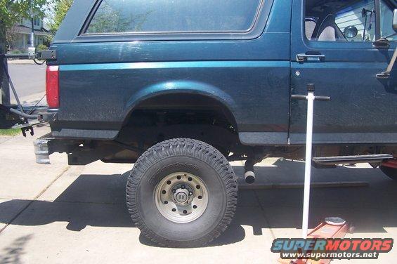 Teal SUV with a body lift, lifted tire, and a jack on the ground
