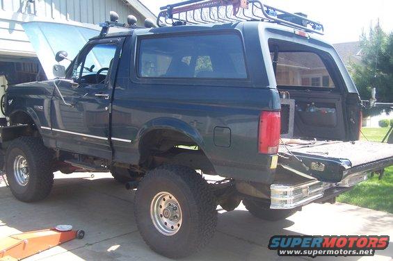 Dark green Ford Bronco with lifted suspension and roof rack. Hood is up, tailgate is open