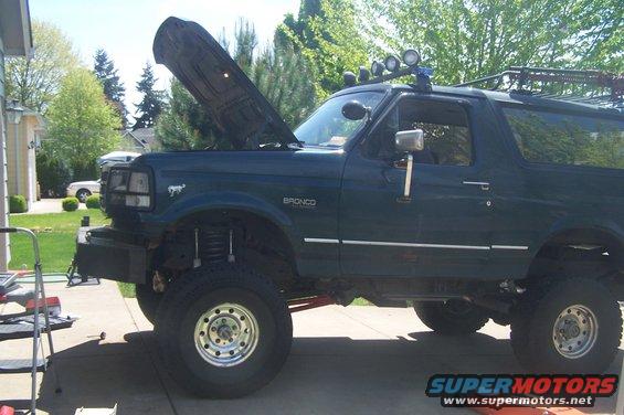Dark green Ford Bronco with hood open, lifted suspension, and roof rack