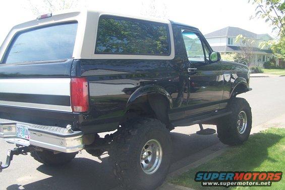 Lifted black and tan Ford Bronco parked on street, side view