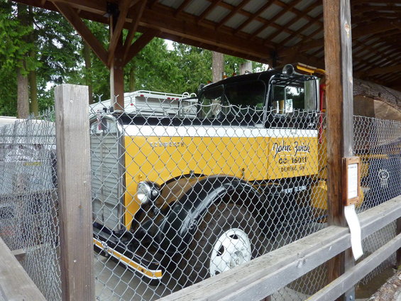 Yellow and black Kenworth truck with 'John Zurich' text on the door, parked under a shelter