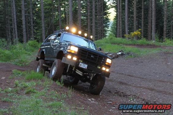 Dark Ford Bronco with roof lights driving on a dirt trail in a forest