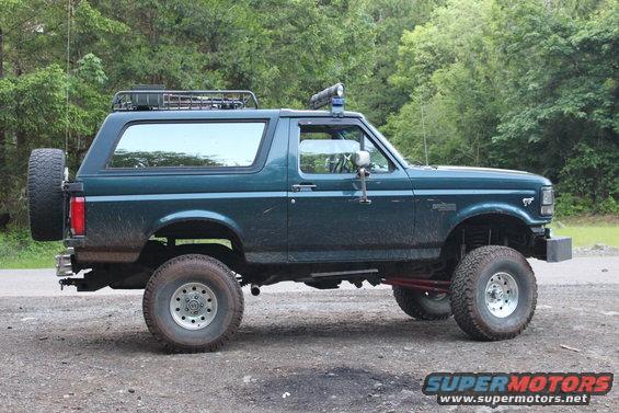 Dark green Ford Bronco, lifted, with roof rack and spare tire, parked on dirt road