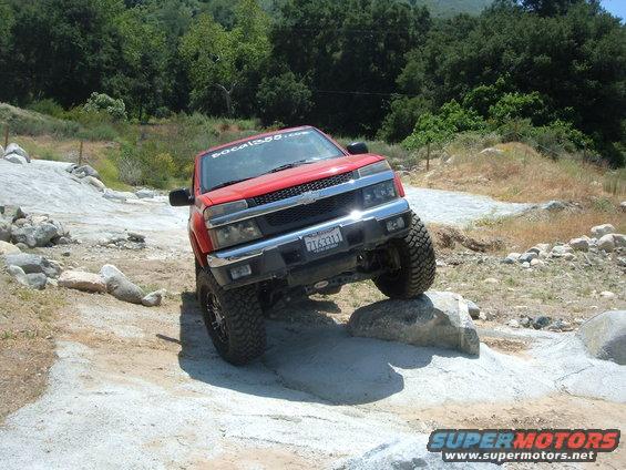 Red Chevrolet Colorado pickup truck with lifted suspension navigating rocks on an off-road trail