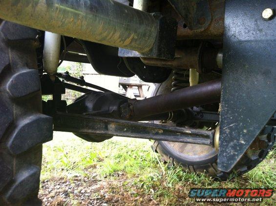 Undercarriage of a vehicle with large tires, showing suspension and drivetrain components