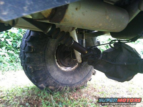 Underside view of a vehicle's rear axle, driveshaft, and tire