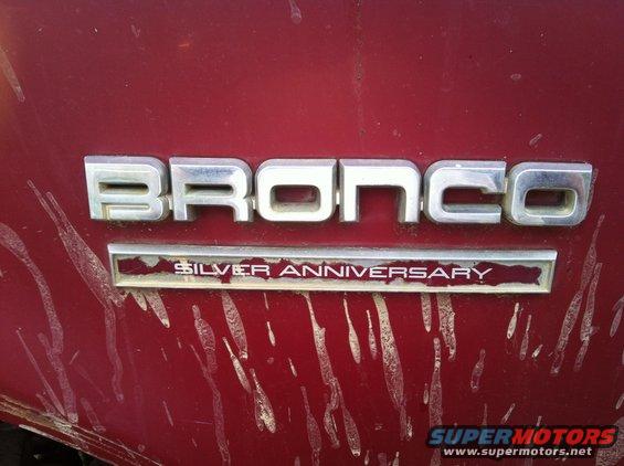 Red vehicle panel with chrome 'BRONCO' emblem and 'SILVER ANNIVERSARY' badge below, showing dirt streaks
