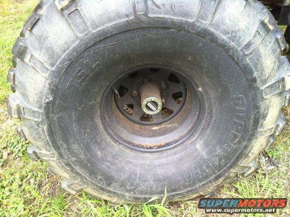 Close-up of a large off-road tire with 'TSL' and 'SUPER' visible, mounted on a black wheel with a metal hub