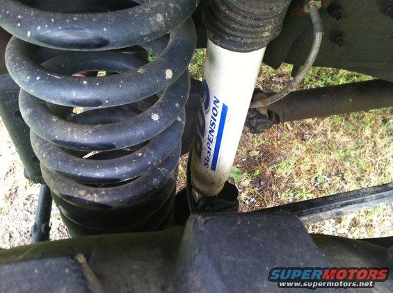 Close-up of a vehicle's coil spring and white shock absorber with blue lettering