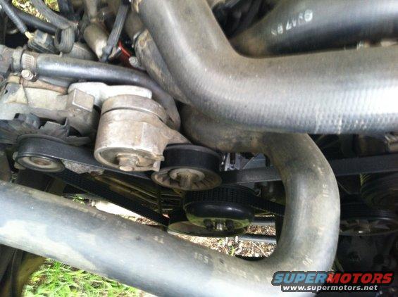 Engine belt tensioner and pulleys with hoses and belts. Some text is visible on hoses