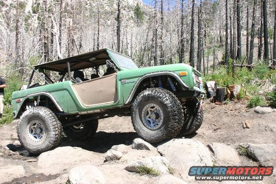 Green off-road Bronco on rocks, removable top, lifted suspension