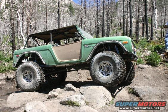 Green Ford Bronco modified for off-roading, climbing over rocks on a trail