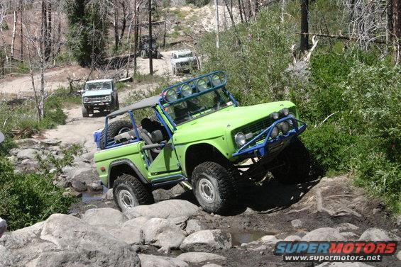 Green Ford Bronco navigating rocks on a trail, with two other Broncos behind it