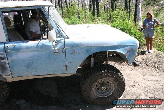 Light blue Ford Bronco with a white roof, lifted suspension, and off-road tires, parked on a dirt road