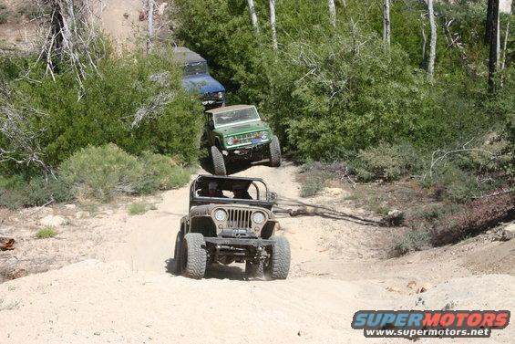 Green 1991 Ford Bronco driving on a dirt trail behind a Jeep