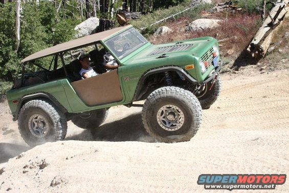 Green Ford Bronco with a soft top driving on a dirt trail, kicking up dust