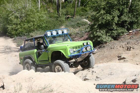 Green Ford Bronco with blue roll cage and lights driving on a dirt trail