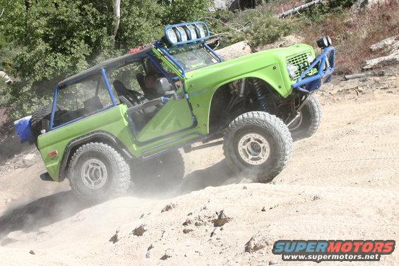 Green off-road SUV with a blue roll cage driving on a dirt hill