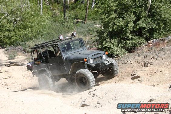 Off-roading in a dark green Toyota Land Cruiser FJ40 on a dirt trail