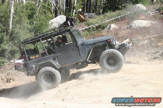 Black off-road vehicle with a roll cage driving on a dirt path, kicking up dust