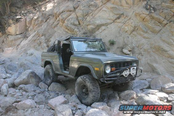 Green Ford Bronco with off-road tires navigating a rocky trail
