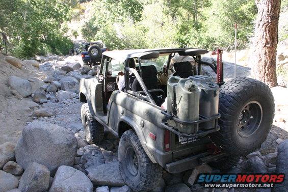 Olive green Ford Bronco with two jerrycans on the rear, driving on a rocky trail