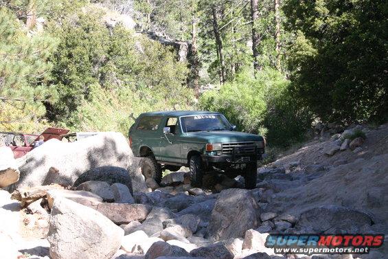Green SUV navigating rocky terrain, "ABUSED" sticker on windshield