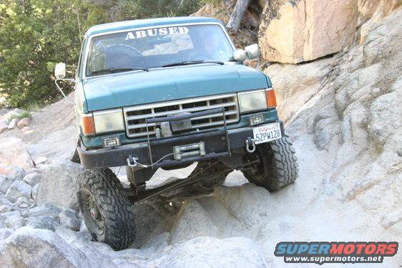 Teal 1991 Ford Bronco off-roading, front view. Winch and "ABUSED" sticker visible