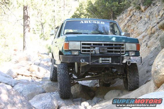 Green 1991 Ford Bronco on rocky terrain with "ABUSED" windshield banner
