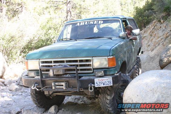 1991 Ford Bronco with 'ABUSED' banner on windshield navigating rocky terrain
