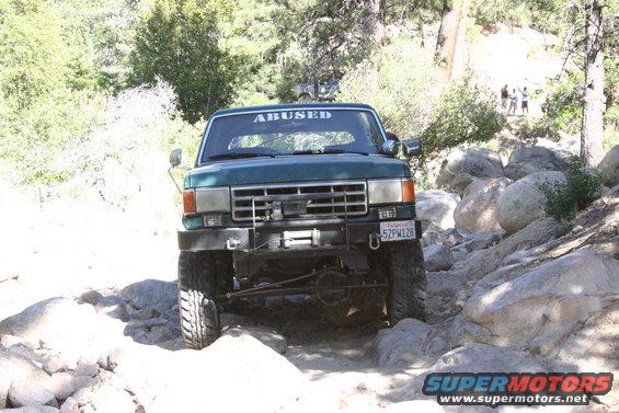 Green Ford Bronco with "ABUSED" sticker on windshield driving on rocky terrain