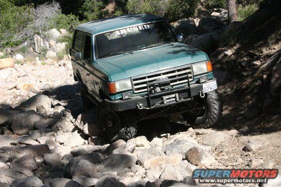 Green SUV with "ABUSED" windshield banner navigating a rocky trail