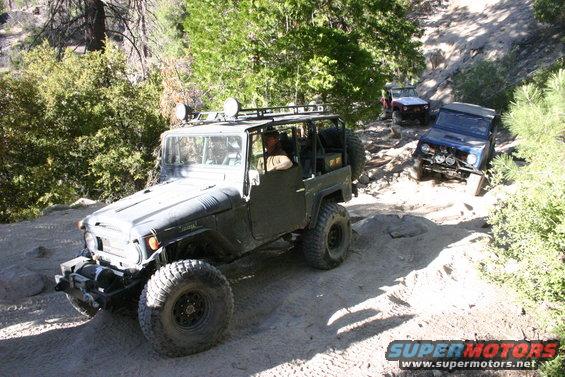 Olive green Toyota Land Cruiser FJ40 on a rocky trail with two other off-road vehicles behind it