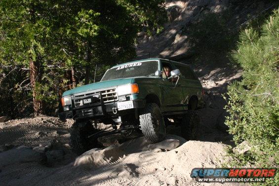 Green Ford Bronco off-roading on a rocky trail, front bumper and grille visible