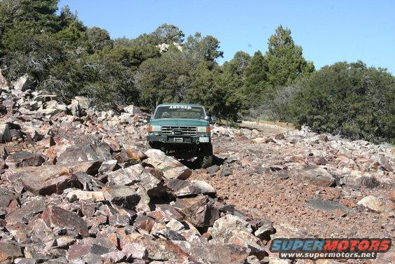 green truck driving over rocks on a trail, has 'ABURR' sticker on windshield